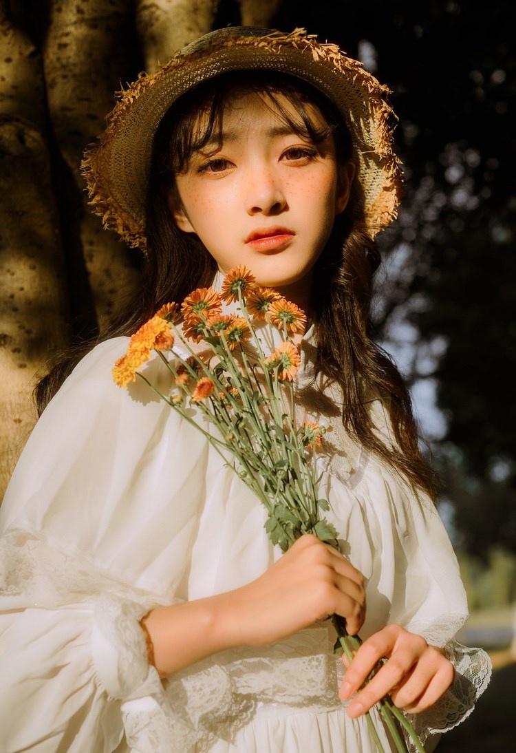 文藝美女潔白長裙濃密卷發手捧鮮花叢林寫真圖片