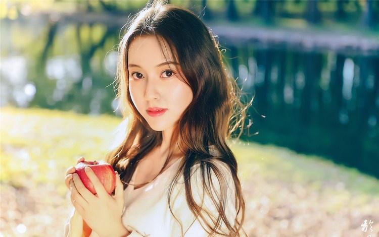 大樹下清純靈動美女手捧蘋果纖細身形圖片