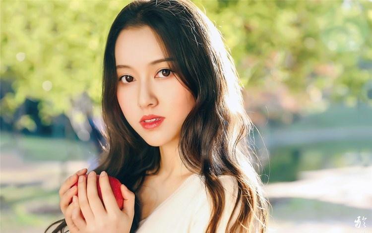 大樹下清純靈動美女手捧蘋果纖細身形圖片